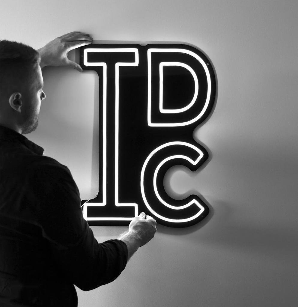 A person positioning an illuminated LED neon sign on a plain wall, holding it level with both hands